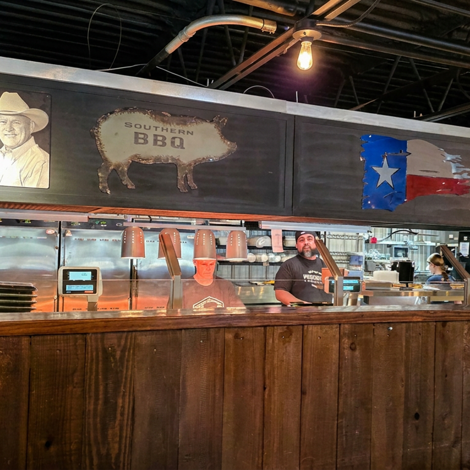 Southern barbecue restaurant counter with staff, food service equipment, and Texas and American flag decorations.